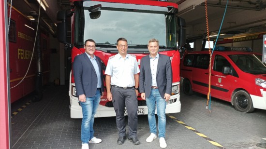 Sebastian Penno, Kai Reichelt und René Kopka in der Feuerwehrtechnischen Zentrale des LK Northeim vor einem Feuerwehrauto